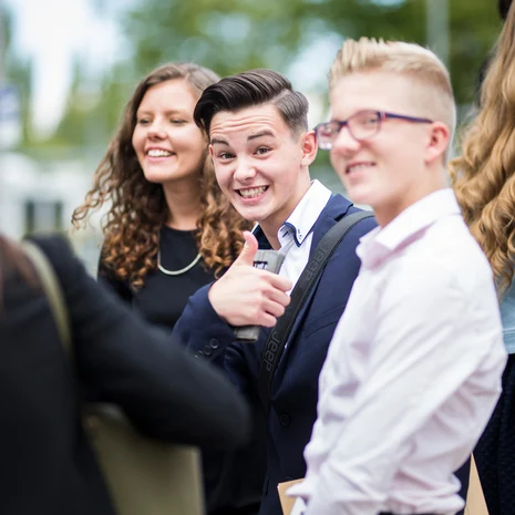 Praktikum Ein Junge der zwischen anderen Personen steht schaut in die Kamera und zeigt lächelnd den Daumen nach oben.