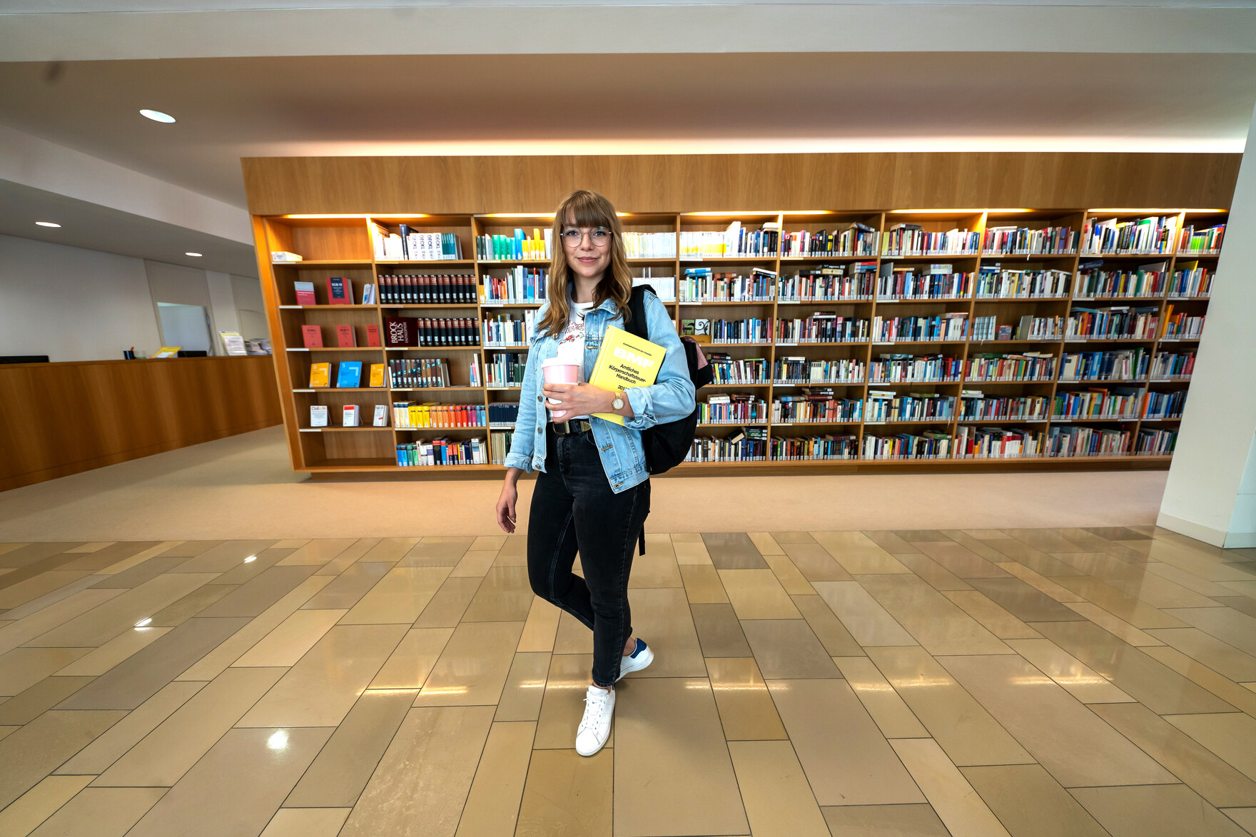Junge Frau mit Fachbuch in einer Bibliothek.