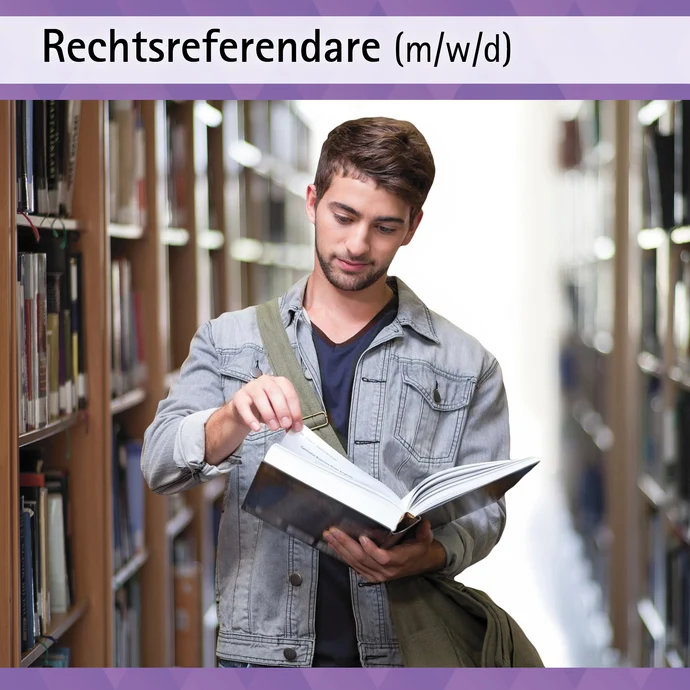 Auf dem Bild ist ein junger Mann in einer Bibliothek abgebildet. Er hält ein aufgeschlagenes Buch in seiner Hand und scheint zu recherchieren. Dieses Bild bildet einen Rechtsreferendaren ab.